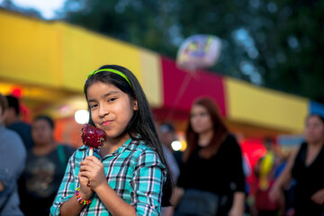 A happy girl holding a caramel apple at a fair.