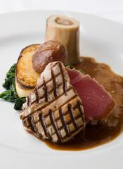 Seared Tuna steak, with beef marrow, spinach, date, potato cake and a beef and wine sauce on a white plate.