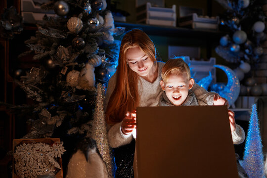 Girl and boy opening Christmas gift at home with New Year 2023 decorations. Christmas. Happiness. Caucasian kids, sister and brother are celebrating winter holidays. High quality image