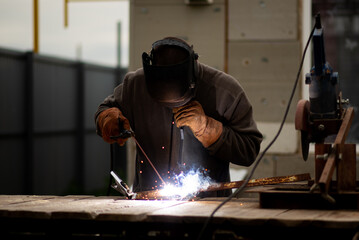 The man works with a welding machine. He is wearing a welder's protective mask and protective...