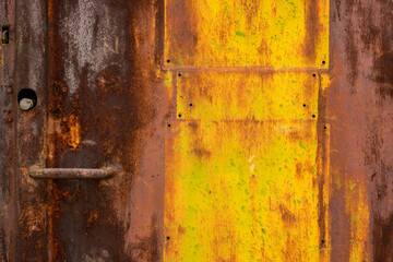 Background rusty sheet metal with yellow and green paint residues and small holes part of an old door with handle and lock