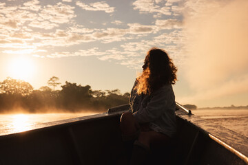 Turista viajando en bote mientras mira el amanecer en rio Madre de Dios  - obrazy, fototapety, plakaty