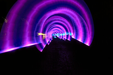 Pink, purple glowing shiny tunnel of light trails effect with yellow and blue streaks on black...