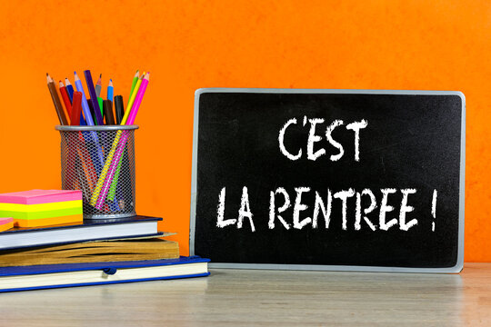 Back to school concept - blackboard with french word : c'est la rentr&eacute;e with pencil-box and books, notebook and sticky note on wooden table