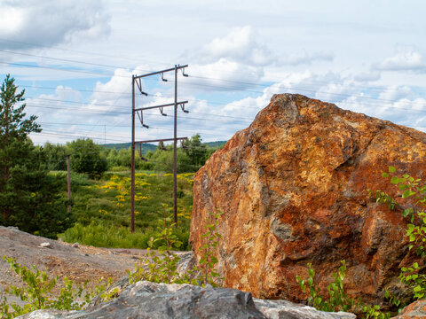 Large orange rock in front of vintage electric wiring in summer landscape Falu Gruva Sweden World Heritage