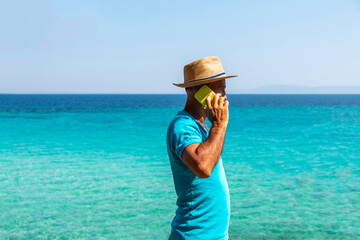 Happy mature man talking by mobile phone next to beach. Business trip