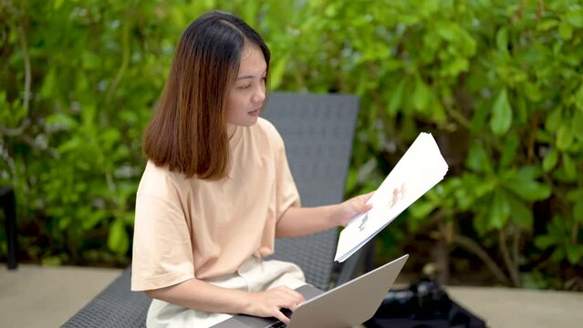 4K, close-up A woman working at the swimming pool with her laptop computer holding paperwork in her hand. It is imperative for young Asian female tourists to sit and work on vacations at the hotel.