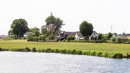 Fototapeta premium Windmill and houses along the river De Linge near the Dutch village of Zoelen in the Betuwe.