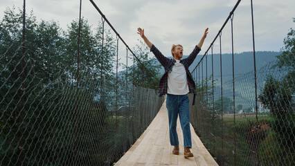 Fototapeta na wymiar Carefree guy explore nature on mountains river bridge. Excited hiker enjoy walk.