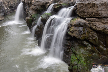 Foaming river water flows down large black rocks in the middle of a tropical forest