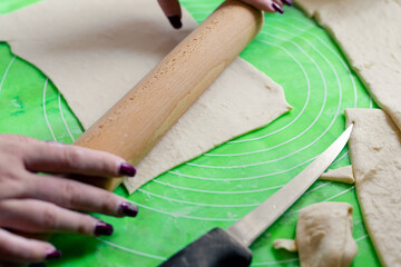 A woman rolls out dough with a wooden rolling pin. Rolling out dough before baking