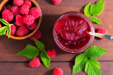 fresh raspberry jam in a glass jar on a wooden table, next to fresh raspberries. concept of homemade jam, preserves for winter, selective focus