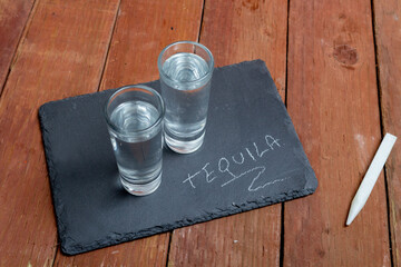 2 shots of tequila on a stone plate with the word tequila written on it