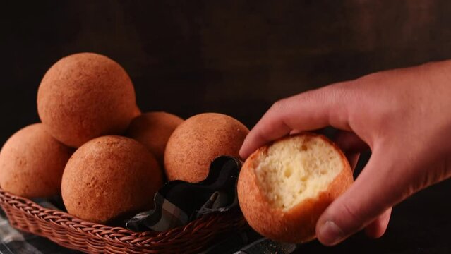 Hand taking a round colombian traditional food named bu&ntilde;uelo in a basket on black wooden table 