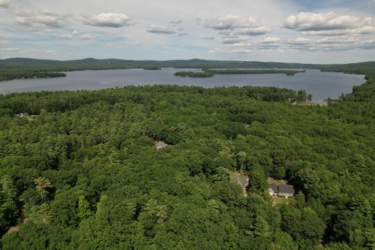 Aeral view of Waukewan Lake in New Hampshire in the middle of a forest and clouds in the background