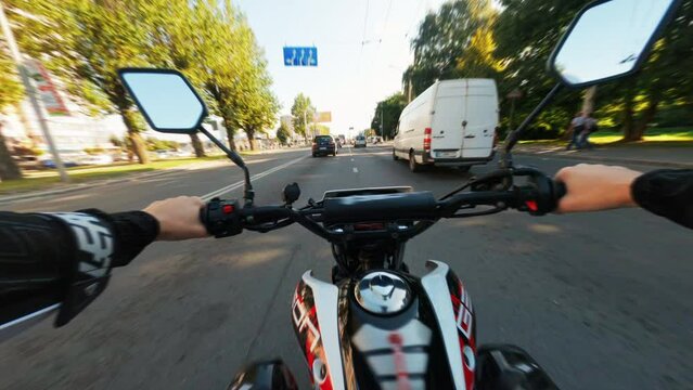 Close-up of male hands of motorcyclist. Urban lifestyle scene. Fast drone FPV. Man riding on scooter over streets in city. Travelling on vehicle. First person view.