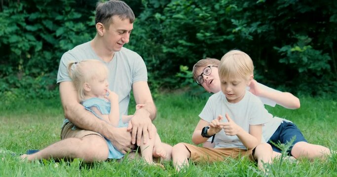 Father spending time with two sons and small daughter outside in the park. Young dad with three kids in park on picnic.