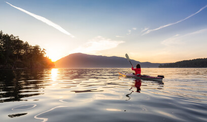 Adventurous Woman on Sea Kayak paddling in the Pacific Ocean. Sunny Summer Sunset. Taken near...