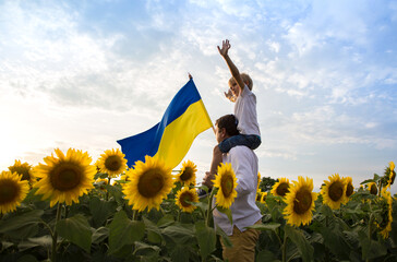 dad with son, who sits on his shoulders, with large flag of Ukraine among a blooming field with...