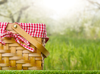 Against the backdrop of summer nature, a straw, beautifully decorated picnic basket on a green lawn. The concept is rest and picnic. Banner, poster, advertising, invitation.