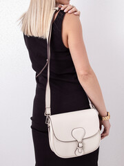 White leather women's handbag with a long strap. Woman in black dress. Romantic clothes for date
