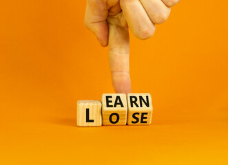 Learn or lose symbol. Concept words Learn and Lose on wooden cubes. Businessman hand. Beautiful orange table orange background. Business and Learn or Lose concept. Copy space.