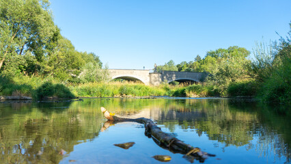 Fototapeta na wymiar Fluss mit Brücke die sich im Wasser spiegelt und einem Baum im Vordergrund