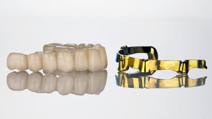 dental prosthesis of the upper jaw from zircon and a gilded bar on white glass with reflection