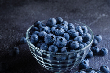 Blueberries organic natural berry with water drops on dark background. Blueberry in glass bowl plate.