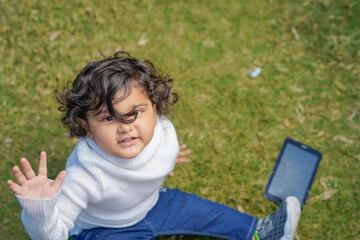 Indian little boy sitting with laptop and tablet in the garden