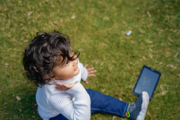 Indian little boy sitting with laptop and tablet in the garden