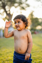 Beautiful baby with curly hair in the garden without t-shirt