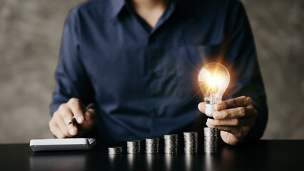 Businessman holds a glowing light bulb on top of the highest pile of coins, Placing coins in a row from low to high is comparable to saving money to grow more. Money saving ideas for investing in fund