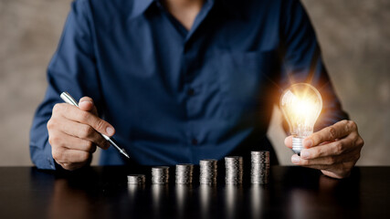 Businessman holds a glowing light bulb on top of the highest pile of coins, Placing coins in a row from low to high is comparable to saving money to grow more. Money saving ideas for investing in fund