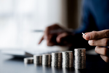 Business man putting a coin on a pile of coins. Placing coins in a row from low to high is comparable to saving money to grow more. The concept of growing savings and saving by investing in stock
