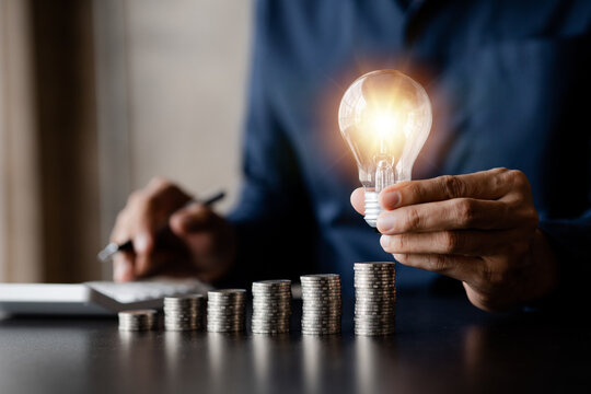 Businessman holds a glowing light bulb on top of the highest pile of coins, Placing coins in a row from low to high is comparable to saving money to grow more. Money saving ideas for investing in fund
