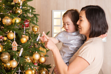 cute baby with down syndrome decorate the Christmas tree with mom, merry christmas and happy new year
