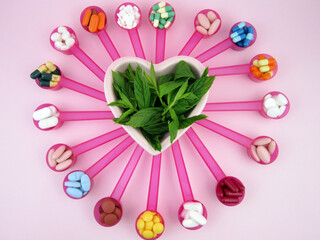  pills, tablets, capsules and herbs in pink spoons        