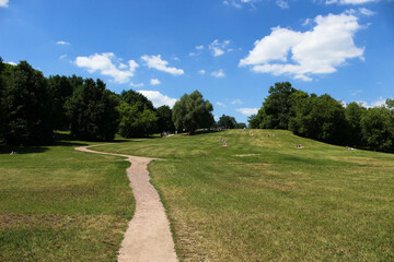 A path in a huge meadow with a green lawn and sunbathing people in the meadow