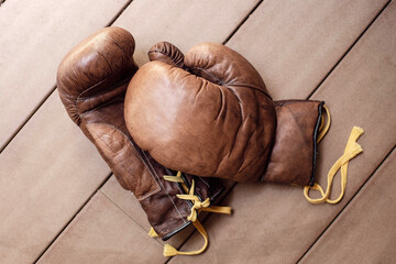 Old worn-out leather brown boxing gloves are on a wooden background.
