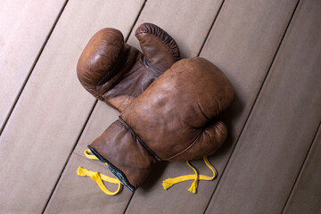 Old worn-out leather brown boxing gloves are on a wooden background.