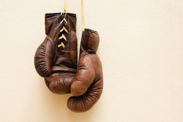 Old worn leather brown boxing gloves hang against the background of the wall in yellow. Copy space..