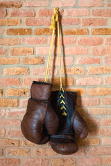 A pair of vintage boxer leather gloves hang against a brick wall. Retro style.	A vertical image.