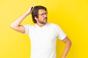 Senior dutch man isolated on yellow background having doubts while scratching head