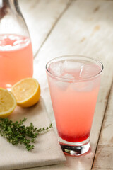 Refreshing cup of pink lemonade with ice, on a wood table