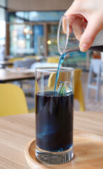 Woman's Hand Pouring Butterfly Pea Flower Tea onto an Ice Cube in a Glass