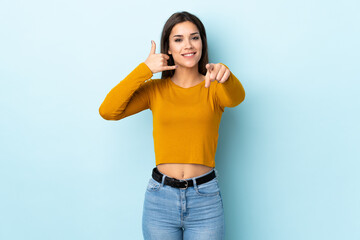 Young caucasian woman isolated on blue background making phone gesture and pointing front