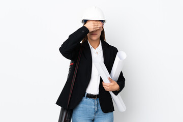 Young architect caucasian woman with helmet and holding blueprints over isolated background covering eyes by hands