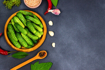 Fresh cucumbers in a wooden plate, spices, herbs, hot peppers, fresh garlic, salt on a dark background with space for text