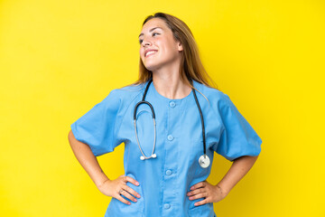 Young surgeon nurse woman isolated on yellow background posing with arms at hip and smiling